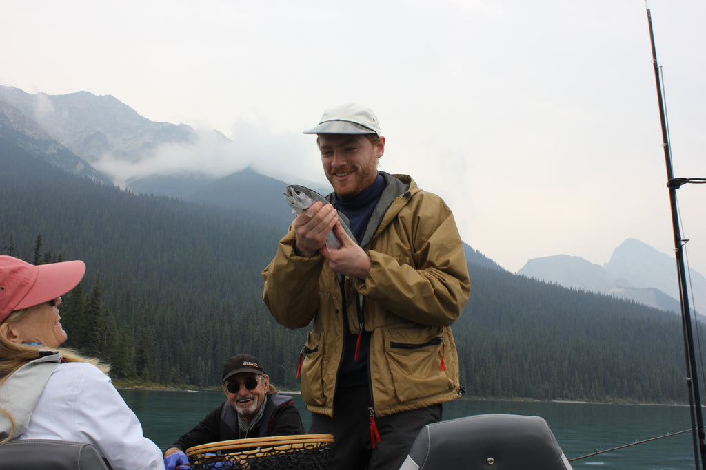 Someone holding a rainbow trout with an oysterman hat and turtleneck sweatshirt one in the Canadian Rockies